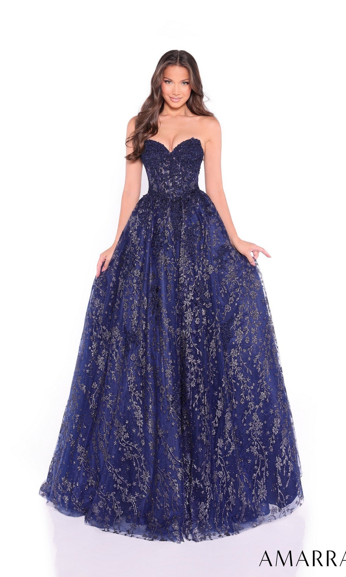 A woman stands against a white background wearing the Amarra 89427 long prom dress, a strapless navy blue ball gown featuring a corset bodice with gold floral detailing.